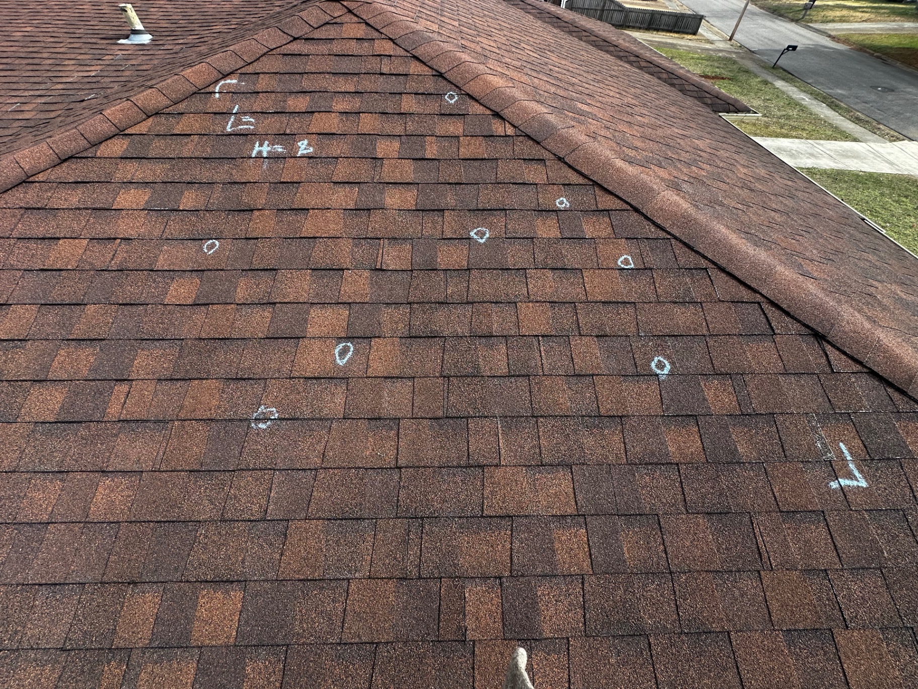 Hail impact marks circled in chalk across a shingle slope during a documented roof inspection