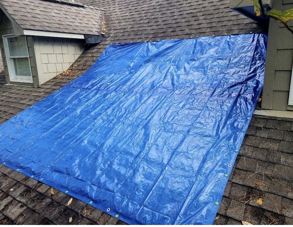 Blue reinforced tarp installed and fastened over a shingle roof section to stop water intrusion