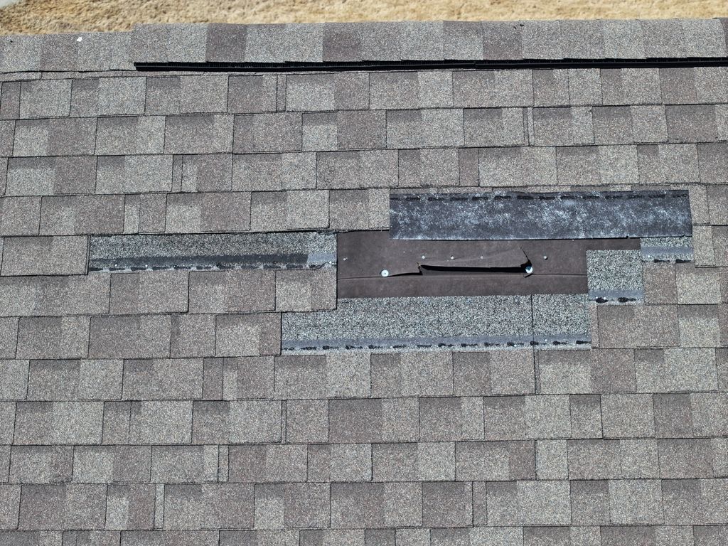 Close aerial view of missing shingles with torn underlayment and exposed fasteners after wind damage