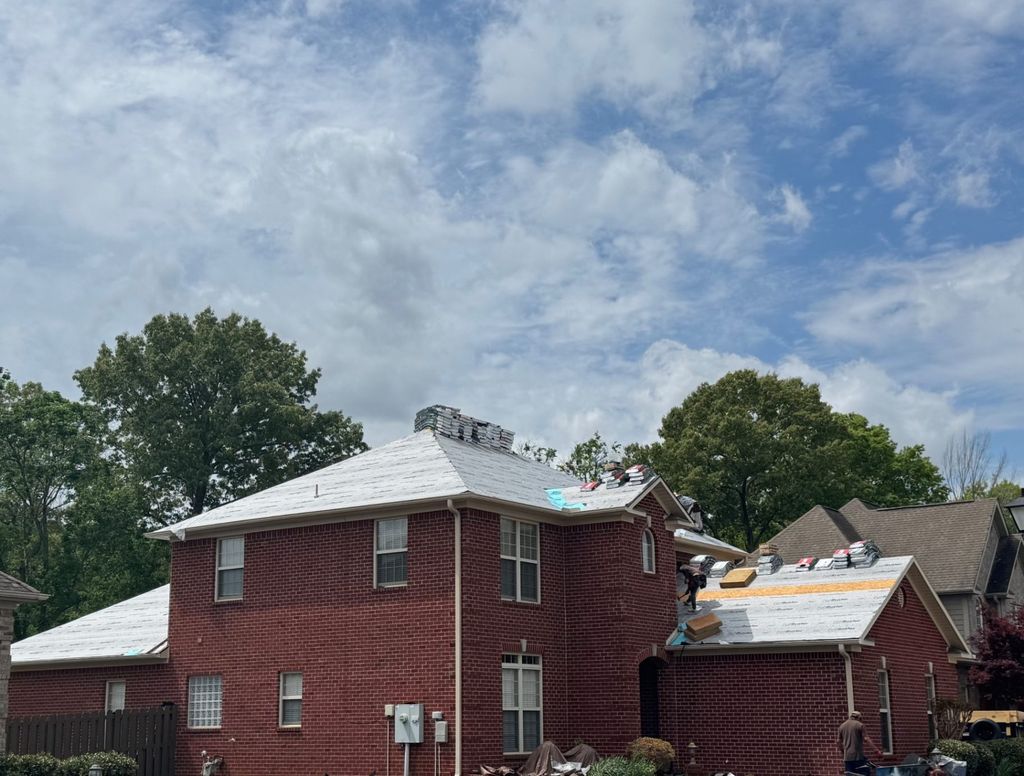 Two-story brick home mid-replacement with synthetic underlayment down and shingle bundles staged on the roof